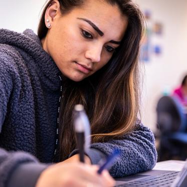 A student in front of a laptop leaning over to write notes