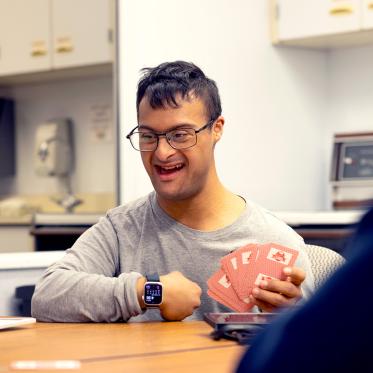 A man smiling while holding playing cards at a table